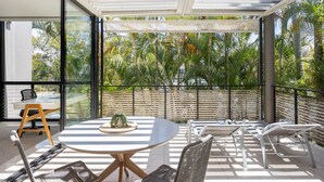 A modern outdoor patio with a round table, chairs, and a glass enclosure. - Luxury Retreat with Private Beach & Jetty (Noosa Heads)