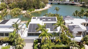 A modern building with solar panels, surrounded by palm trees and a body of water. - Luxury Retreat with Private Beach & Jetty (Noosa Heads)