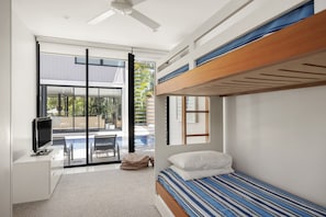 A modern bedroom with a bunk bed, a flat-screen TV, a desk, and a large sliding glass door leading to an outdoor area. - Luxury Retreat with Private Beach & Jetty (Noosa Heads)