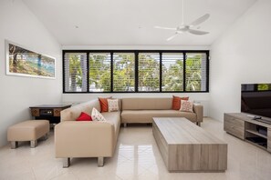 A modern living room with a beige sofa, a coffee table, and a TV. - Luxury Retreat with Private Beach & Jetty (Noosa Heads)