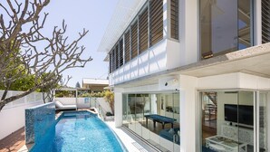 Ein modernes Haus mit Swimmingpool, Glastüren, die auf eine Terrasse führen, und einem Flachdach.