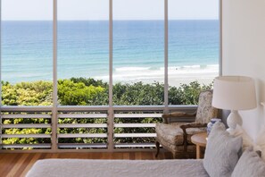 A room with a large window overlooking a beach, a chair, a lamp, and a white textured sofa. - The Beach Shack - Getaway on Sunshine Beach (Sunshine Beach)