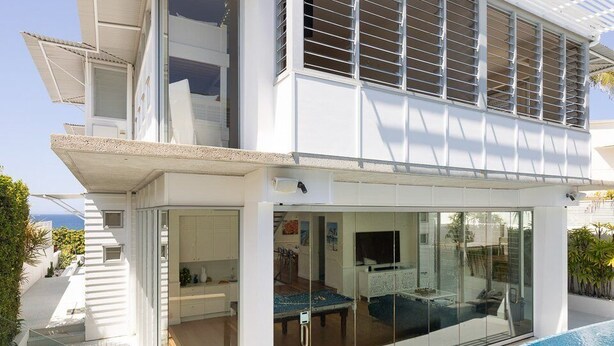 Ein modernes, zweistöckiges Haus mit Schwimmbad, großen Fenstern und einer überdachten Terrasse.