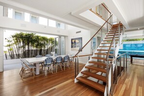 Un vaste espace de vie agrémenté d’un escalier en bois, d’une table à manger avec des chaises et d’une vue sur une piscine.