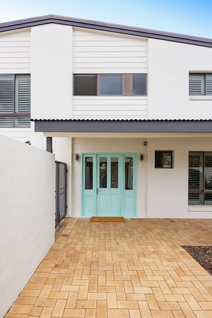 Een modern gebouw met twee verdiepingen, een lichtblauwe deur, een plat dak en een verharde oprit.