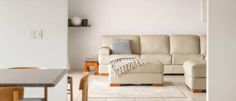 Una sala de estar minimalista con un sofá beige, una mesita de madera y una alfombra blanca.