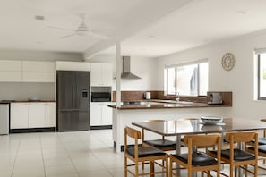 Une cuisine moderne avec des meubles blancs, un réfrigérateur en acier inoxydable, un four encastré et un coin repas comprenant une table et des chaises.