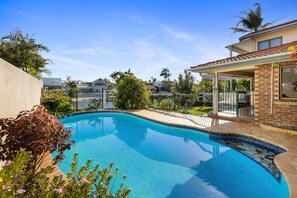 A swimming pool with a tiled edge, surrounded by a fence and various plants.