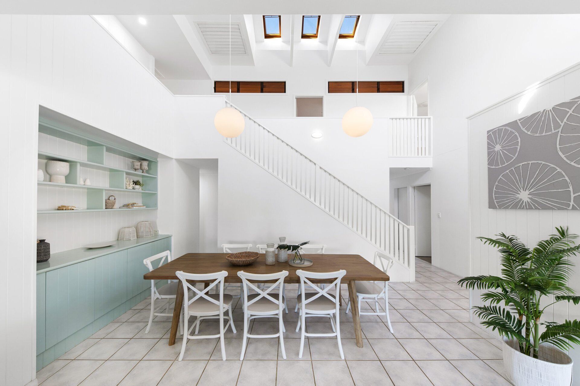 A spacious dining area with a high ceiling, white walls, and a staircase leading to an upper level.