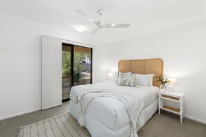 Una camera da letto con un letto, comodini, una ventola a soffitto e vista attraverso una porta scorrevole.
