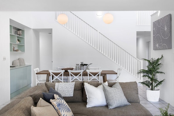 A modern living room with a staircase, a dining area, and a large potted plant.