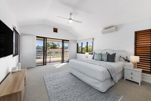 A bedroom with a bed, bedside tables, a ceiling fan, and a view through the balcony doors.