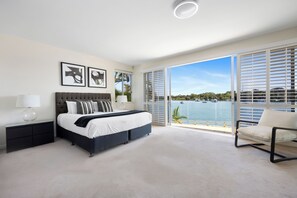 Relax in this serene bedroom with a large bed, nightstand, and window offering a view of the water.