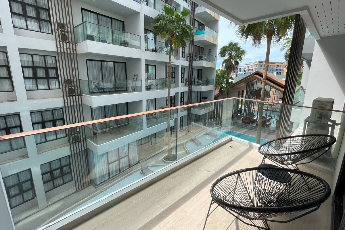 Un immeuble moderne à plusieurs étages, doté de balcons, de rampes en verre et d’un espace extérieur aménagé pour s’asseoir.