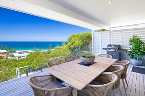 Une terrasse avec une table en bois et des chaises en osier, offrant une vue sur la plage et l’océan.