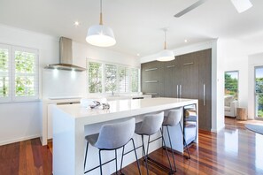 A modern kitchen with a central island, bar stools, pendant lighting, and a view of the outdoors.