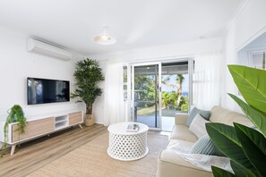 Relax in this stylish living room with a flat-screen TV, comfortable sofa, and sliding glass door leading to a balcony with ocean views.