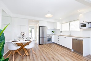 A modern kitchen with white cabinetry, stainless steel appliances, and a wooden floor.