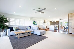 A modern living room with a sofa, coffee table, and a dining area with a kitchen in the background.
