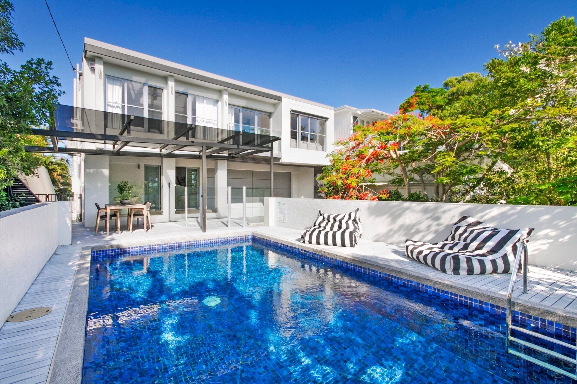 Ein modernes Haus mit Swimmingpool, Sitzgelegenheiten im Freien und einer überdachten Terrasse.