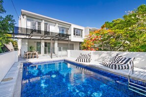 Une maison moderne dotée d’une piscine, d’un espace salon extérieur et d’un patio couvert.