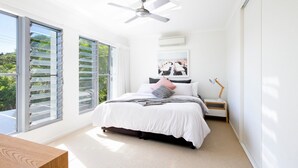 Makuuhuoneessa on sänky, kattotuuletin, yöpöytä, lamppu ja suuri ikkuna, jossa on sälekaihtimet.