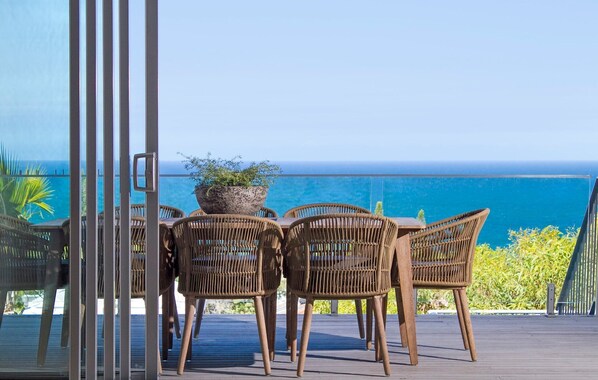 Un balcon avec des fauteuils en osier et une table, donnant sur une mer d’un bleu limpide.