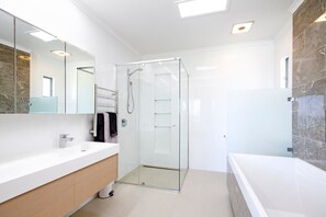 Une salle de bain moderne avec une douche à parois de verre, un meuble-lavabo blanc et un mur recouvert de carreaux de marbre.