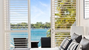 A bedroom with a view of a beach and boats, a bed with a gray blanket, and a black chair. - Luxury Riverfront: Private Pool, Water Views (Noosa Heads)