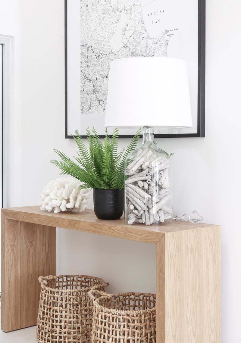 Una consola de madera con una maceta de helecho, una botella de vidrio decorativa y cestas de mimbre.