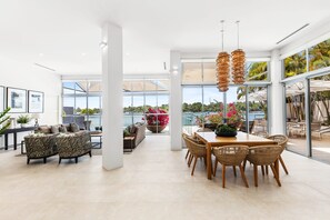 Ampla sala de estar com grande mesa de jantar, assentos confortáveis e janelas grandes com vista para o exterior.