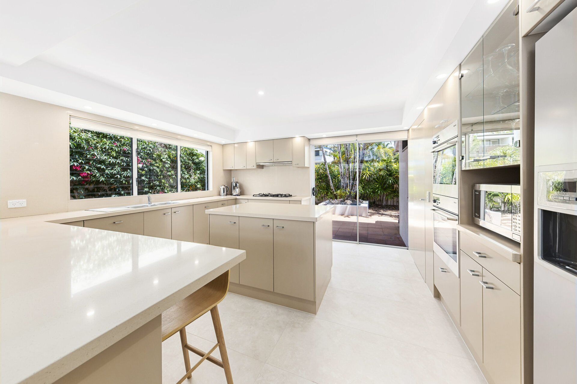 A modern kitchen with a central island, built-in appliances, and a view of the garden.