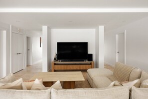 A modern living room with a flat-screen TV on a wooden stand, a beige sofa, and a coffee table. - The River Rest - Noosa Jetty Stay (Noosa Heads)