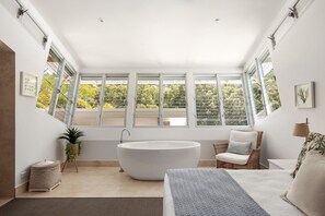 Un baño moderno con una bañera independiente, ventanas amplias y una silla de mimbre.