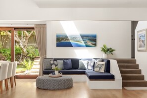 Un saló modern amb un sofà modular, un otomà rodó i una escala.