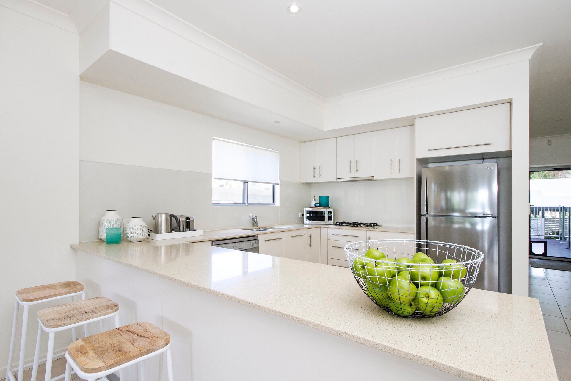 A modern kitchen with white cabinets, a stainless steel refrigerator, a microwave, and a bowl of green apples on the counter.