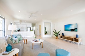 A modern living room with a sofa, coffee table, and a TV on the wall. - Tranquil & Modern Riverside Getaway (Tewantin)