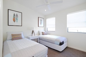 A bedroom with two beds, a bedside table with a lamp, and framed artwork on the wall. - Tranquil & Modern Riverside Getaway (Tewantin)