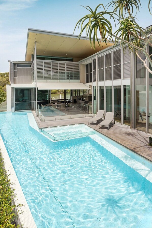A modern two-story house with a swimming pool, outdoor seating, and large windows.