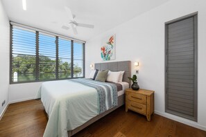Une chambre à coucher avec un lit, une table de chevet et une vue sur un lac, visible à travers de grandes fenêtres.