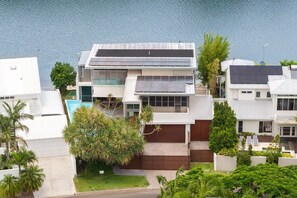 A modern two-story house with a swimming pool, solar panels, and lush greenery.