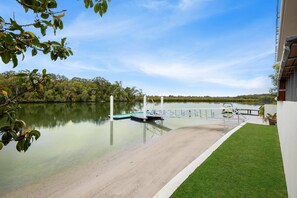 Un lac paisible, avec un quai, une zone herbeuse et un bâtiment à la façade blanche.