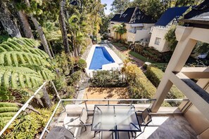 A residential property with a swimming pool, lush greenery, and a balcony with a table and chairs.