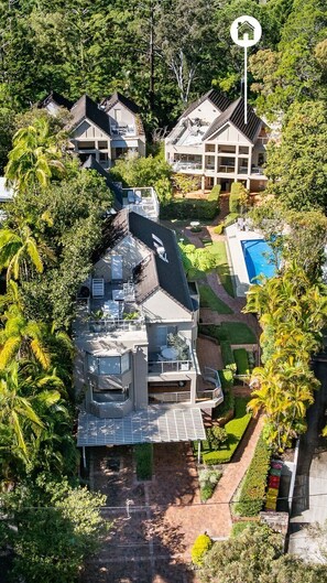 A multi-story residential building with a swimming pool, surrounded by lush greenery and palm trees.