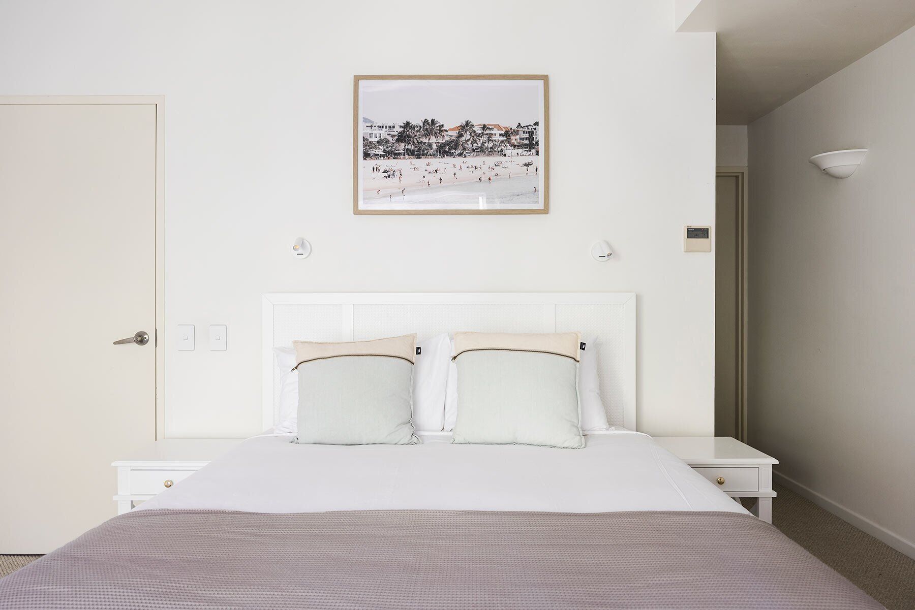 Una camera da letto con un letto, un comodino, un quadro appeso al muro e una porta.