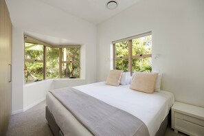 A bedroom with a bed, two windows, a bedside table, and a carpeted floor.