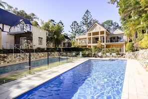 A swimming pool with a stone wall and a glass fence, surrounded by a well-maintained garden and a two-story house with balconies. - Alderly 6 - Calm Little Cove Stay (Little Cove)