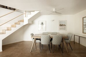 A dining area with a wooden table, four chairs, a ceiling fan, and two framed pictures on the wall.