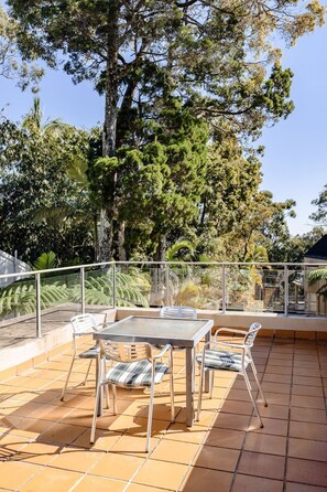 Eine Terrassengruppe mit Tisch und Stühlen, umgeben von einem Geländer und verschiedenen Bäumen.
