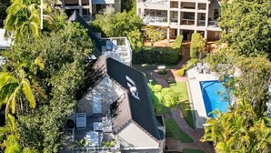 Una casa moderna de varios pisos con piscina, rodeada de abundante vegetación.